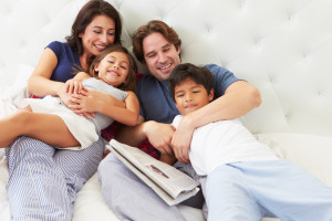 Family Relaxing In Bed With Coffee And Newspaper